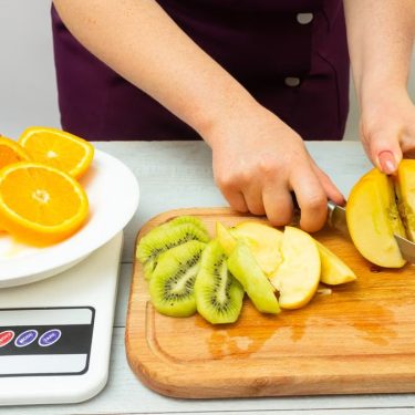 Woman slicing fruits including apple, kiwi, and orange for a healthy meal preparation.